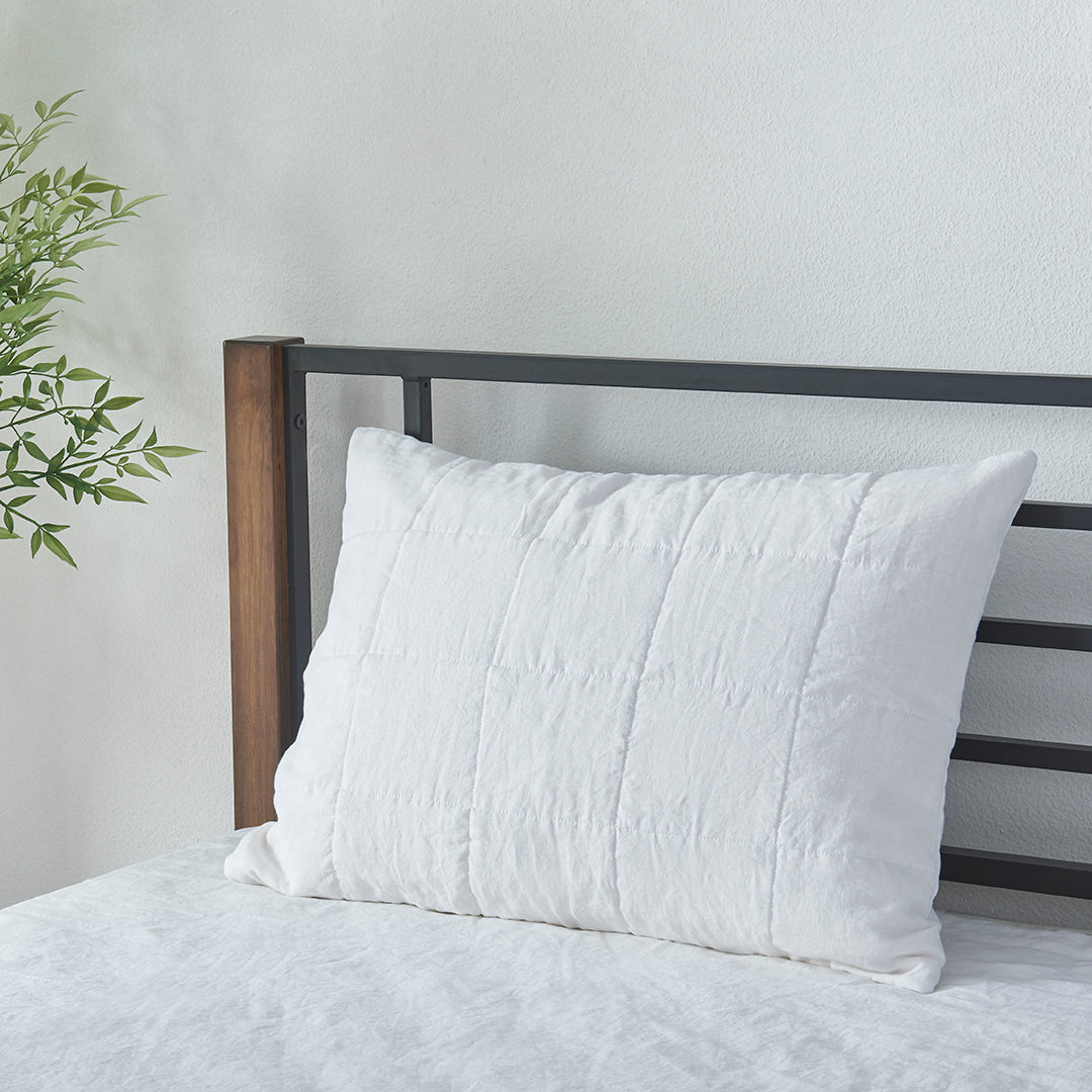 An optic white 100% linen quilted pillowcase propped up against bed headboard